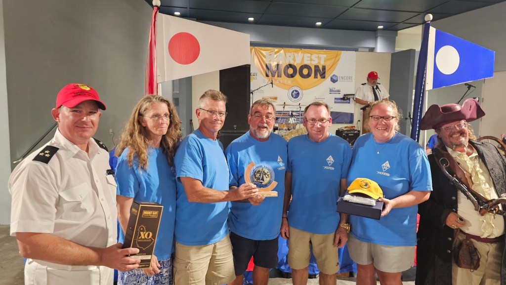 A crowd of sailors celebrating with trophies and drinks at the Harvest Moon Regatta awards party